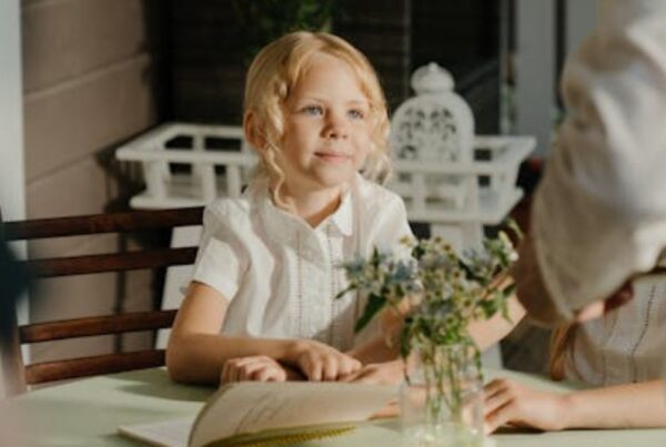 An opened book with a blonde-haired child looking expectant in a sunlit room.