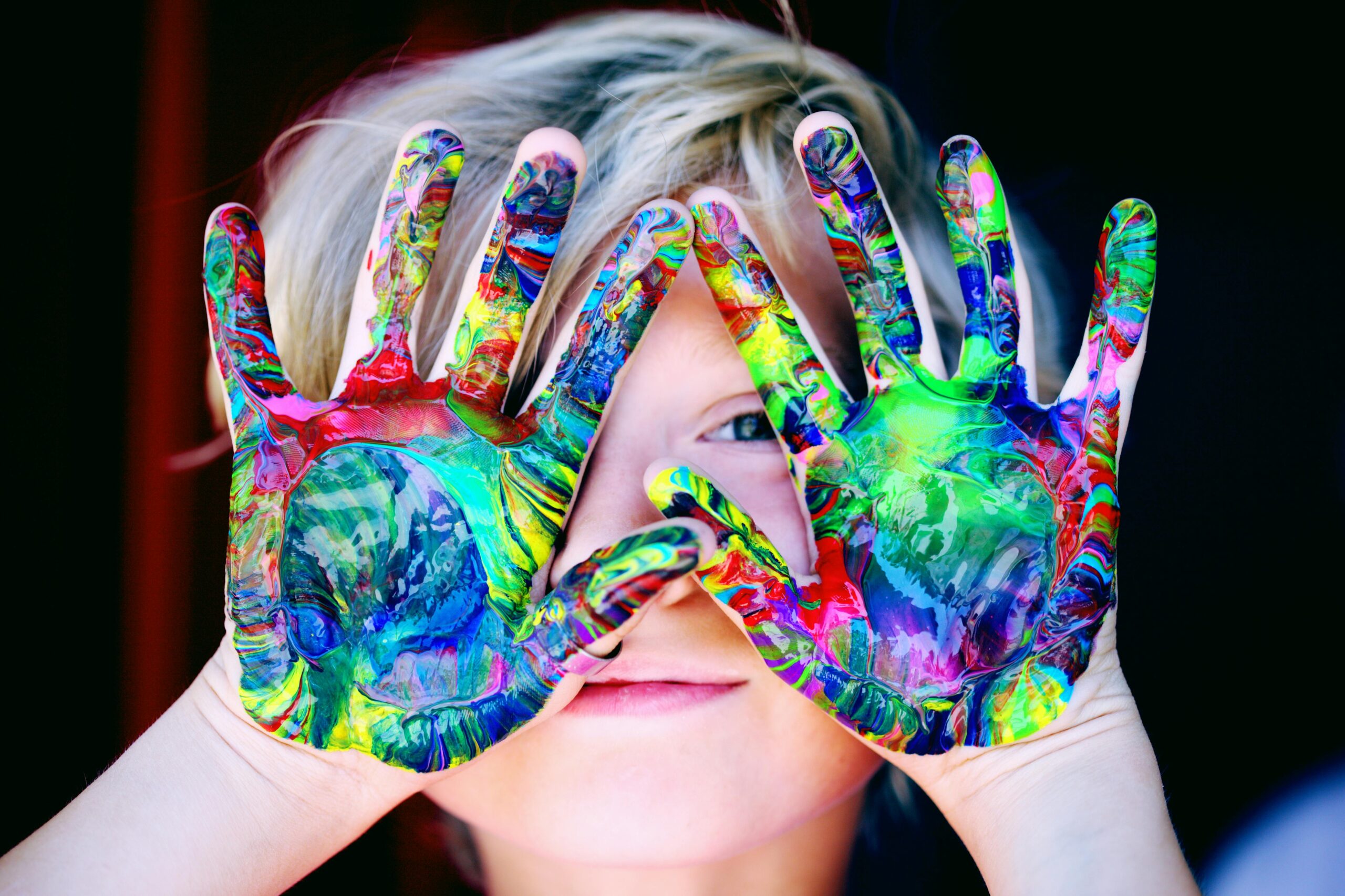 A child with colorful hands playing with paint in rainbow colors, looking happy and self-assured.