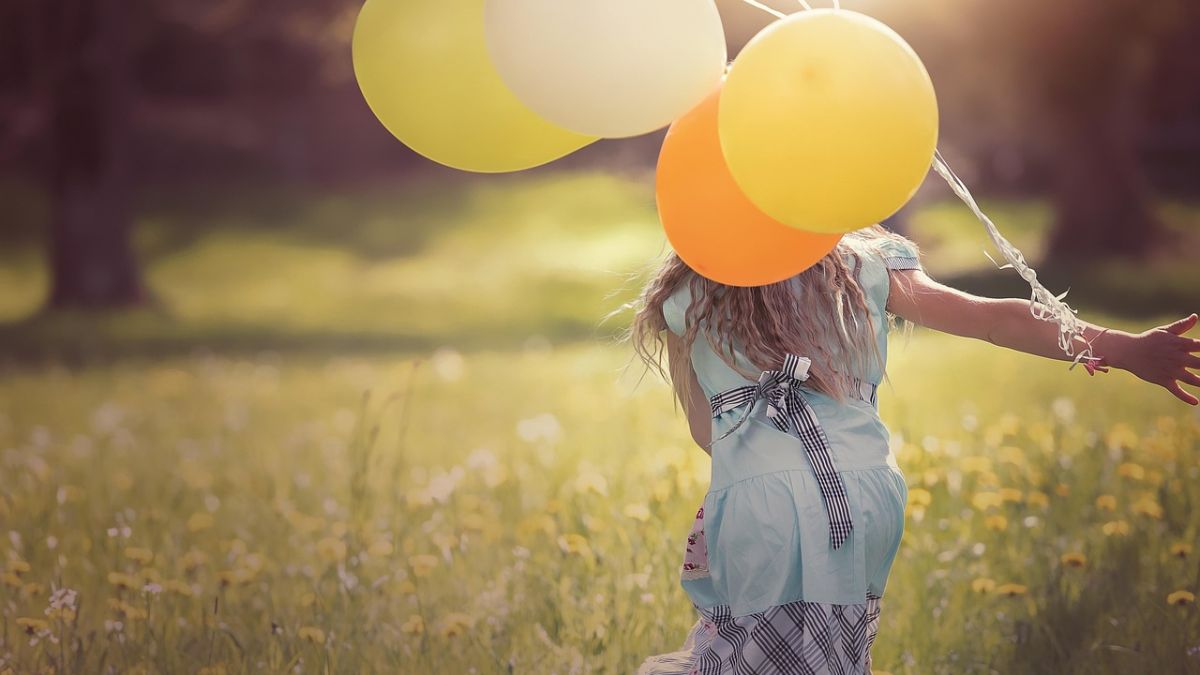 A young girl runs across a meadow holding balloons, her back to the camera, illustrating freedom and play in daily life for a child with autism.