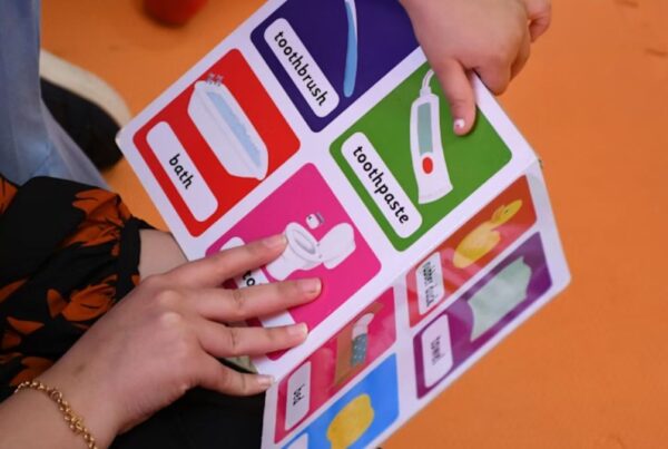 In ABA therapy, a child looks at picture cards used as task signage while only their hands and the therapist’s hands are visible.