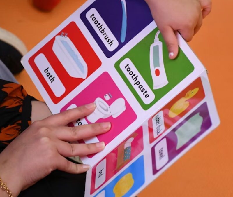 In ABA therapy, a child looks at picture cards used as task signage while only their hands and the therapist’s hands are visible.