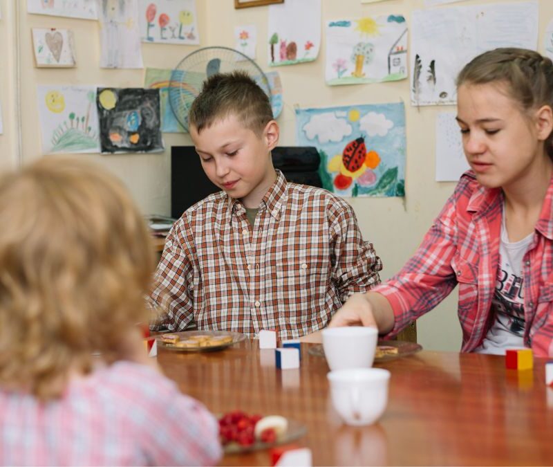 Activities for autism classroom, older children sit around a table with puzzles and toy pieces in front of them during a classroom activity.