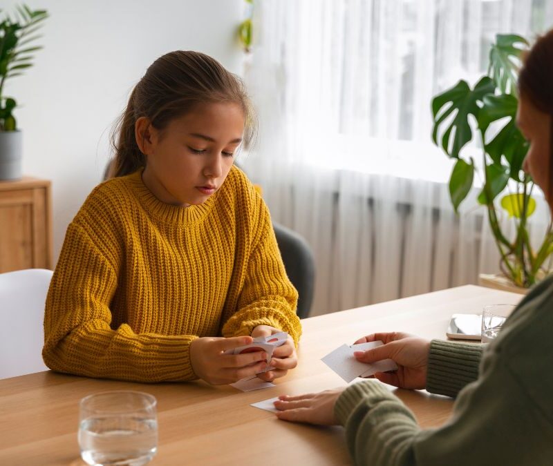A young girl with her eyes downcast speaks to a concerned counselor, reflecting the stigma surrounding autism.
