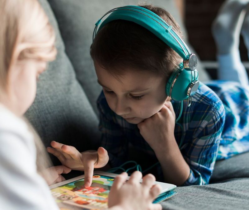A young boy relaxes on a sofa, fully engaged in a puzzle game while listening on headphones, illustrating autism repetitive behavior.