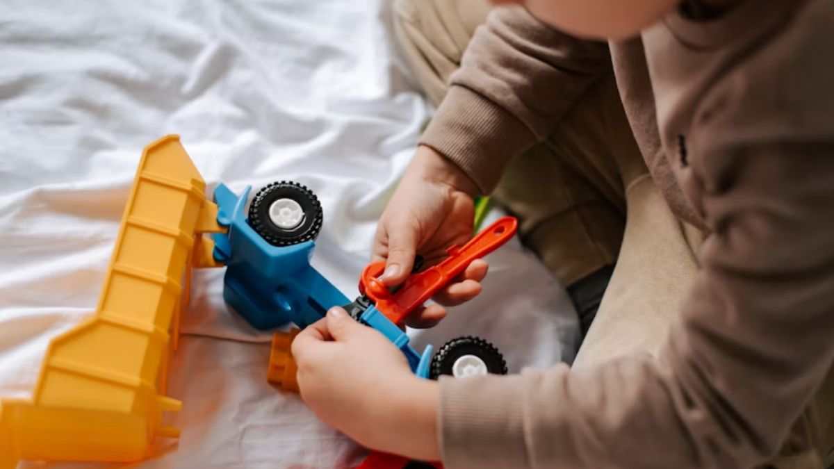 Sensory items autism, a child’s hand fidgets and assembles a plastic toy truck while sitting in a sand pit for tactile play.