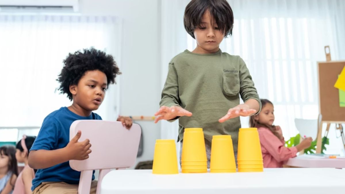 A group of children in a school playroom works together to stack colorful cups during a behavioral therapy session, reflecting current trends that use playful teamwork to build skills.