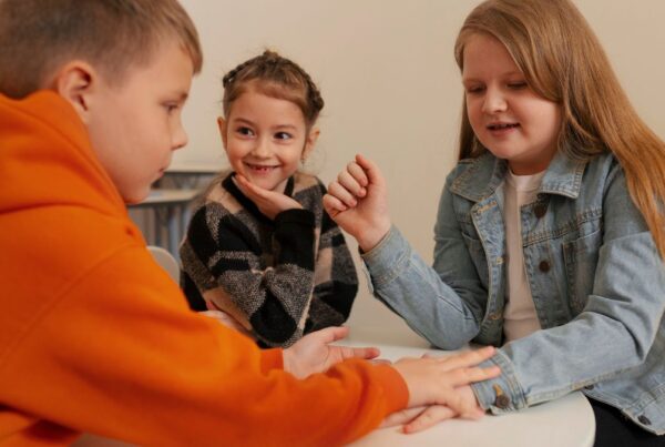 A group of older children sits in a bright therapy room, playing hand-clap games together during a behavioral therapy session, highlighting growing trends in social-skills play.
