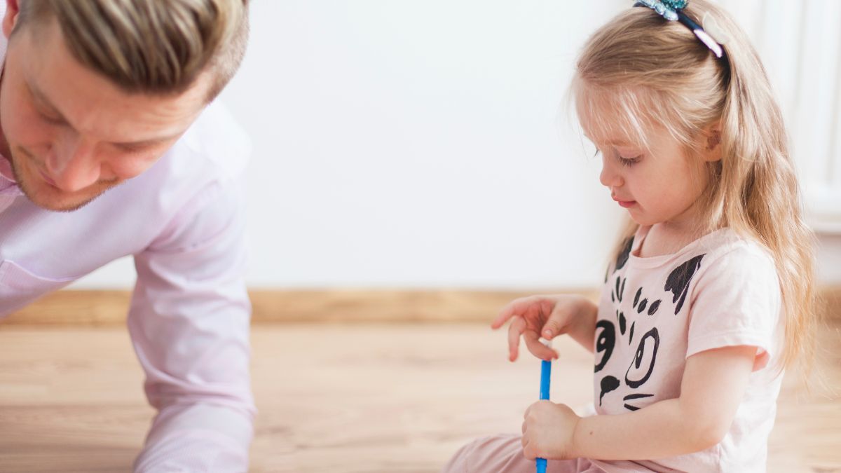 A father guides his child through functional communication training in a brightly lit living room.