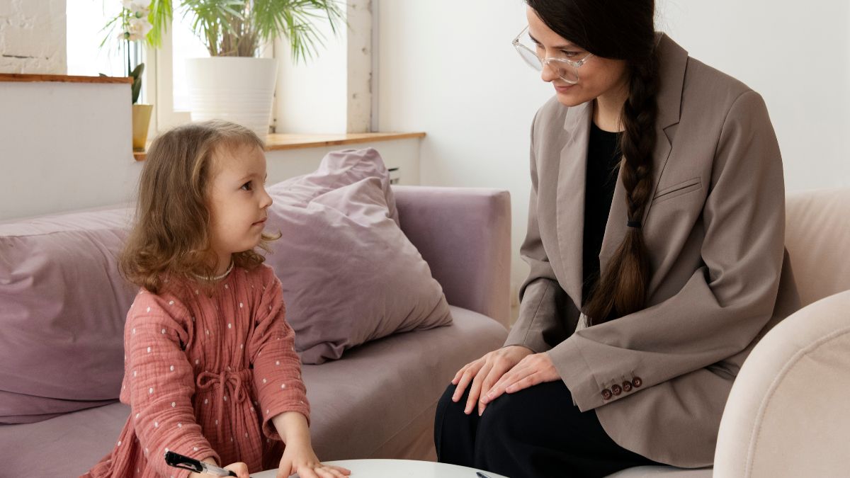 A young girl shows early signs of autism as a female therapist guides her during a therapy session.