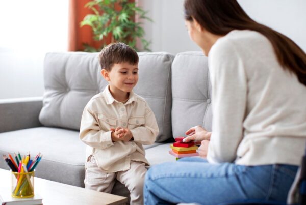 A therapist guides a child through a functional communication training activity in their living room during in-home ABA therapy.