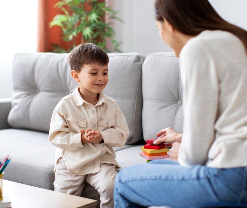 A therapist guides a child through a functional communication training activity in their living room during in-home ABA therapy.
