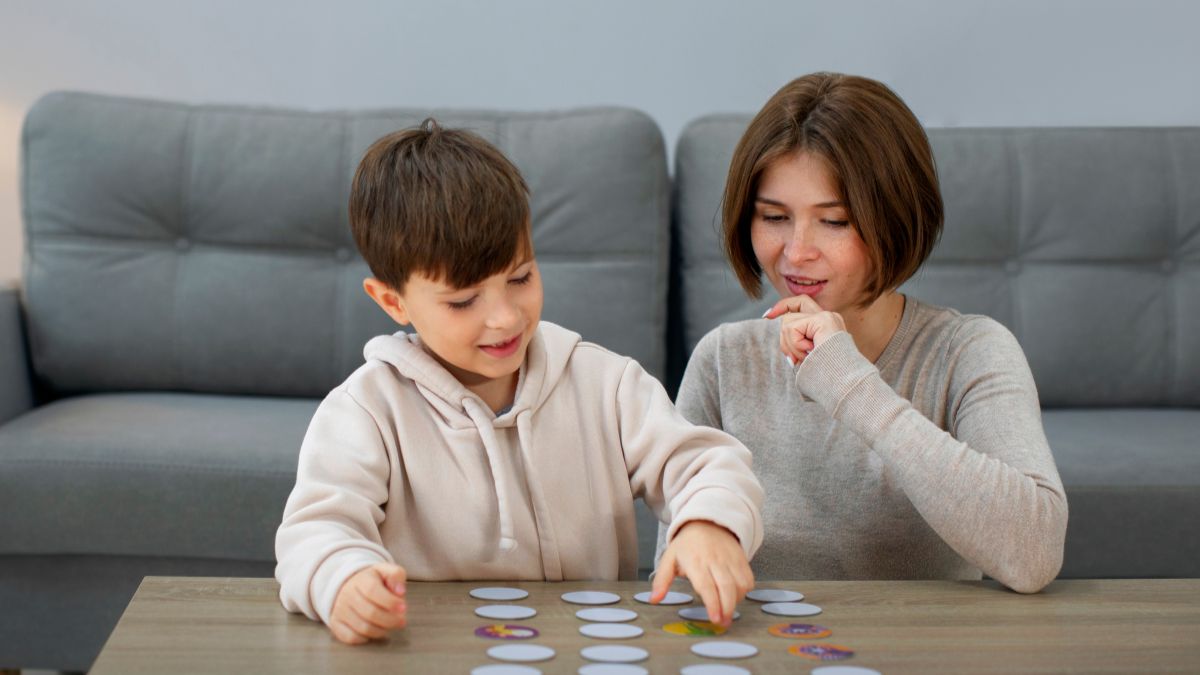 A female therapist guides a young boy in a picture emotion card activity during functional communication training.