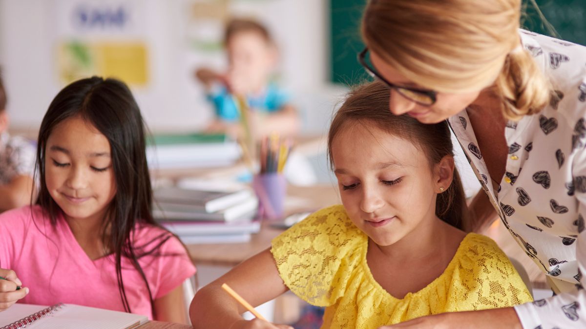 A therapist closely guides two children as they work on a writing activity at a table during ABA therapy at home.