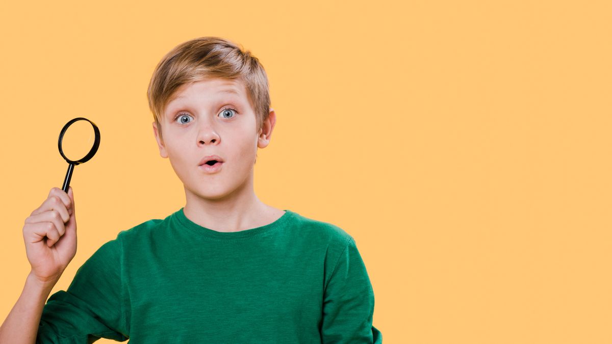 A young boy with autism holding a magnifying glass, looking surprised.